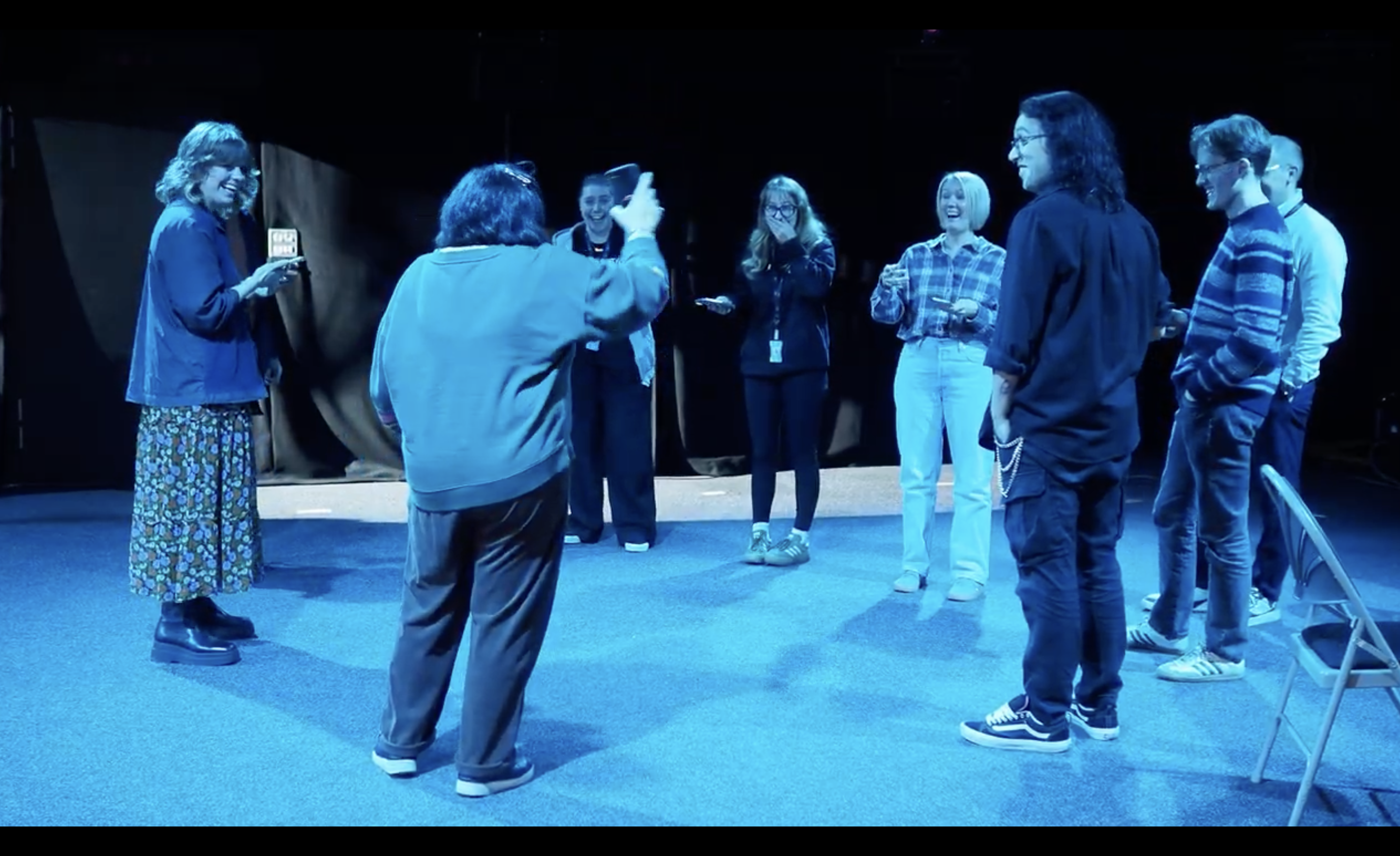 A circle of collaborators in a blue-lit rehearsal space hold their phones as Tendril reads motion data from each device.